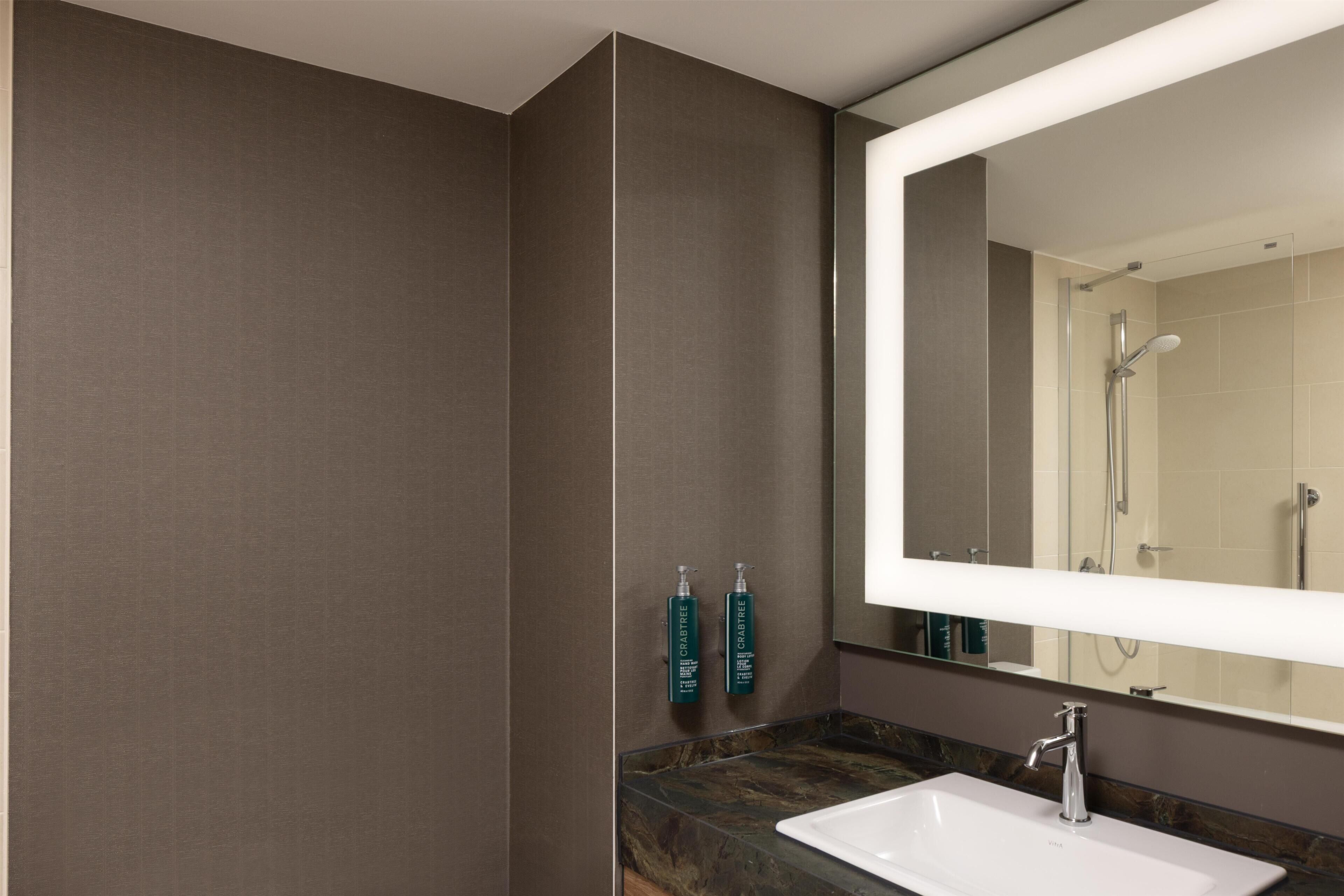 Un baño moderno con un espejo grande, un lavabo y dos botellas verdes en la pared.