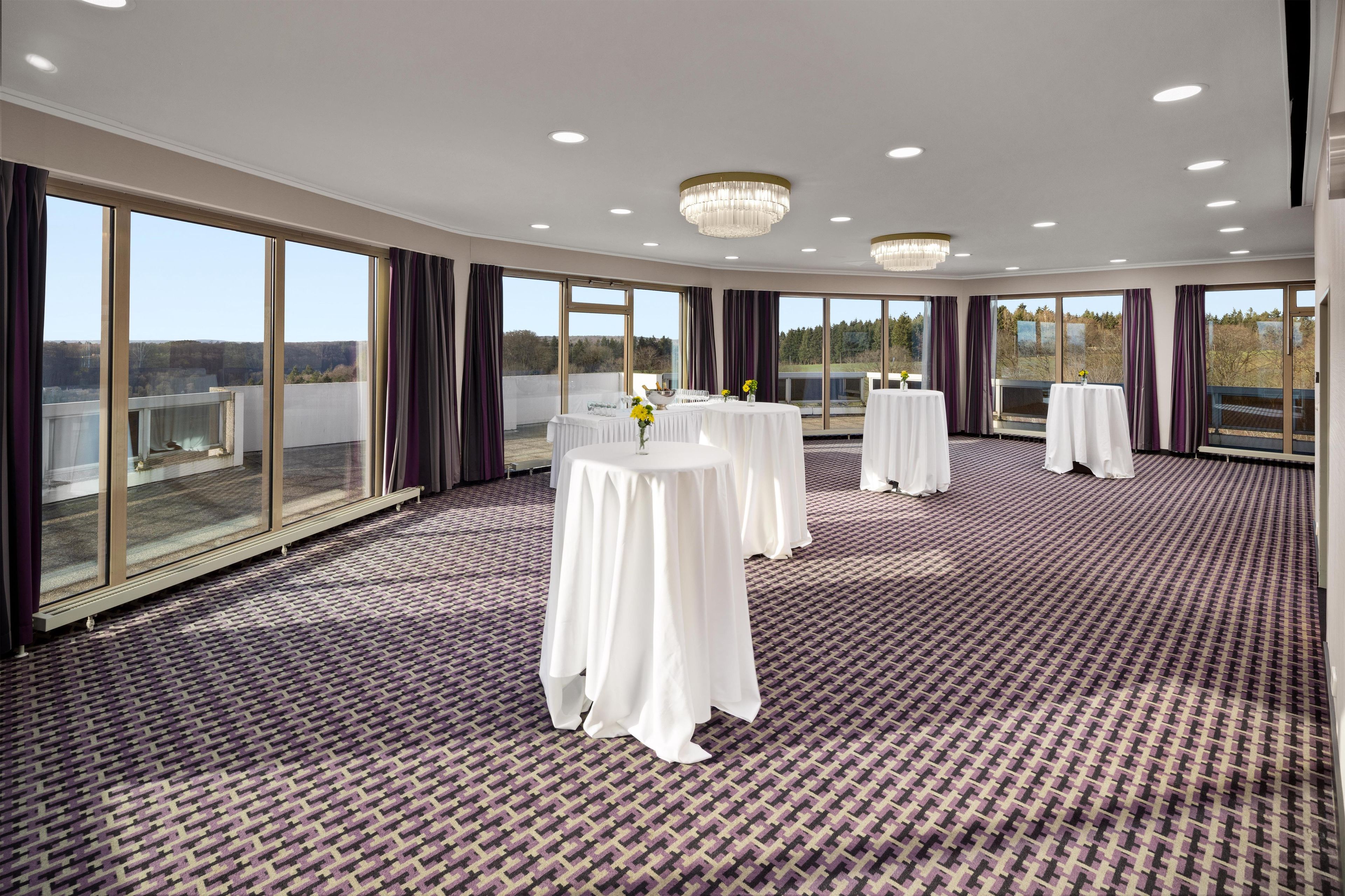 A conference room with large windows, round tables, and a patterned carpet.