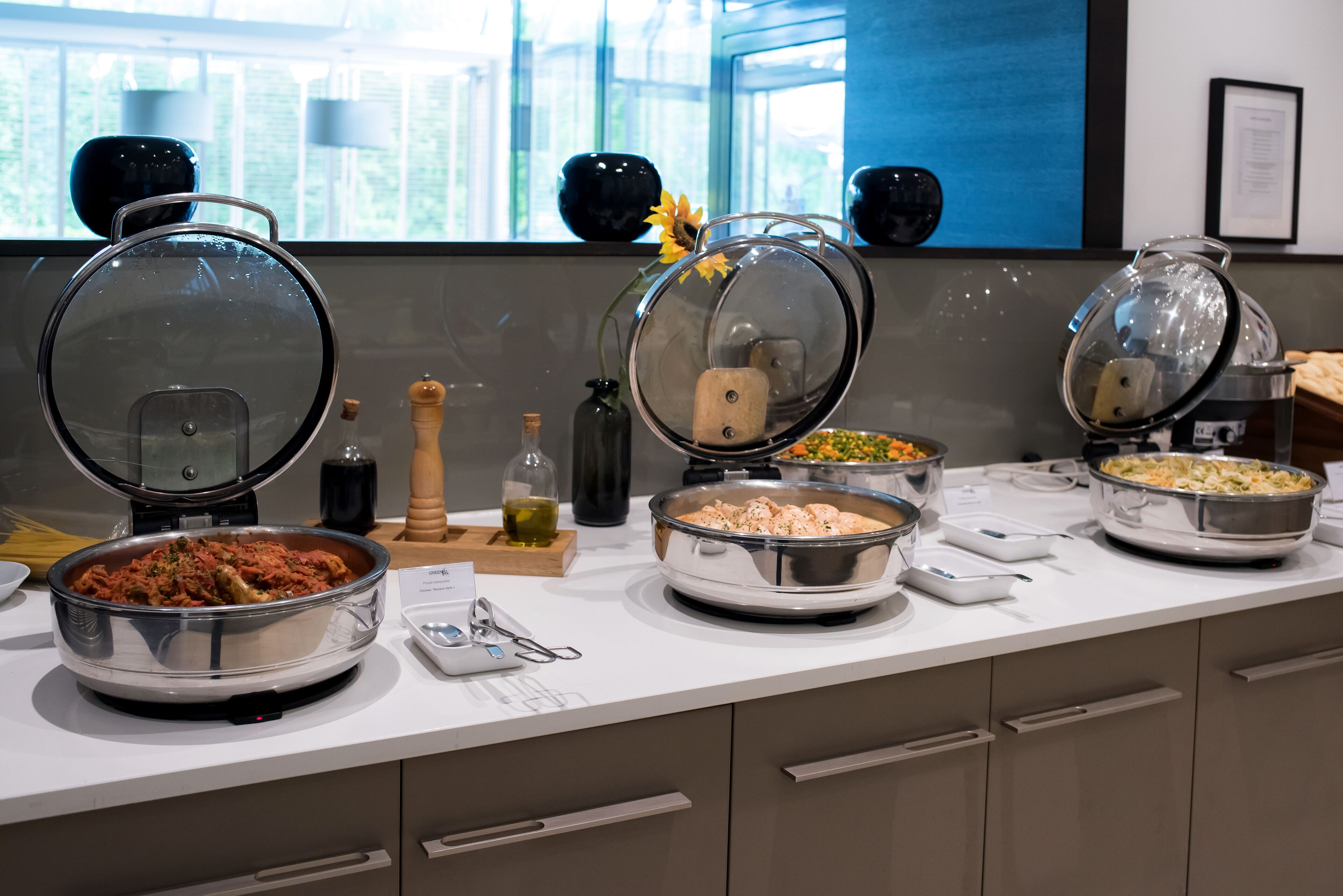 Un buffet proposant une variété de plats, une fenêtre avec vue et un vase décoratif orné d’un tournesol.