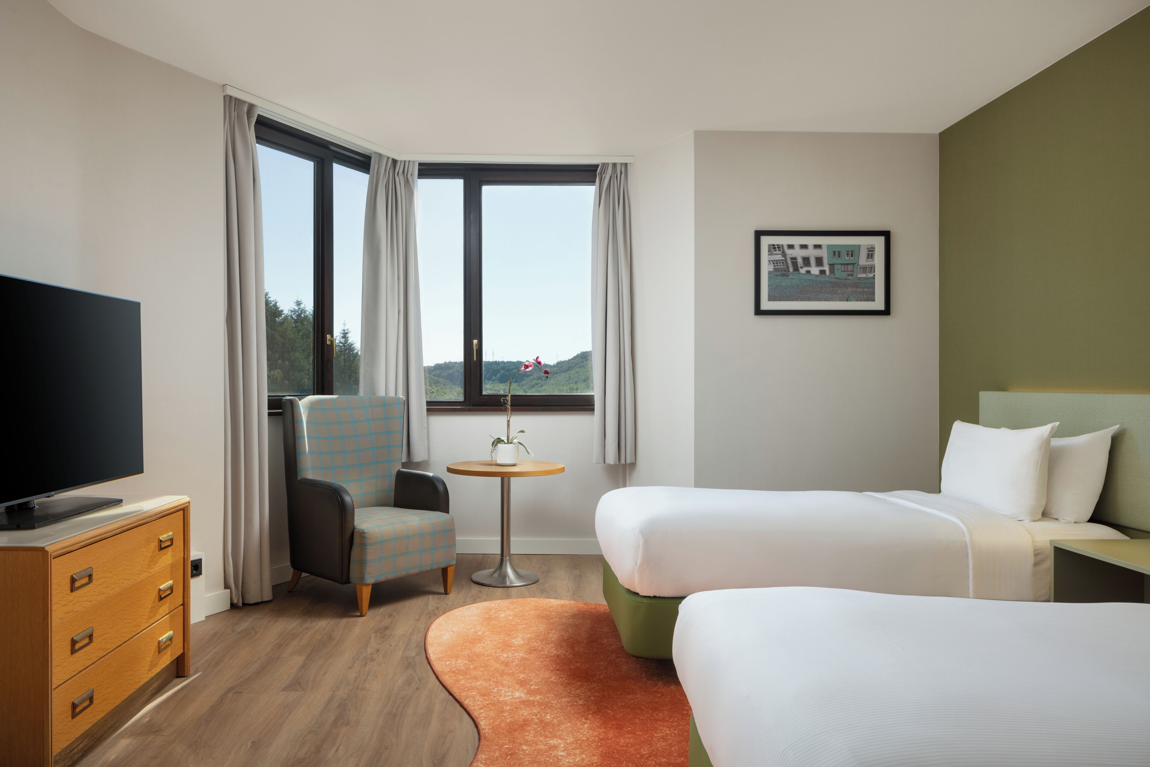 Une chambre d’hôtel équipée d’une télévision, de deux lits, d’une chaise, d’une petite table et d’une fenêtre donnant sur un paysage agréable.