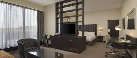 A hotel room with a large bed, a desk with a chair, a sofa, a television, and a window with curtains.