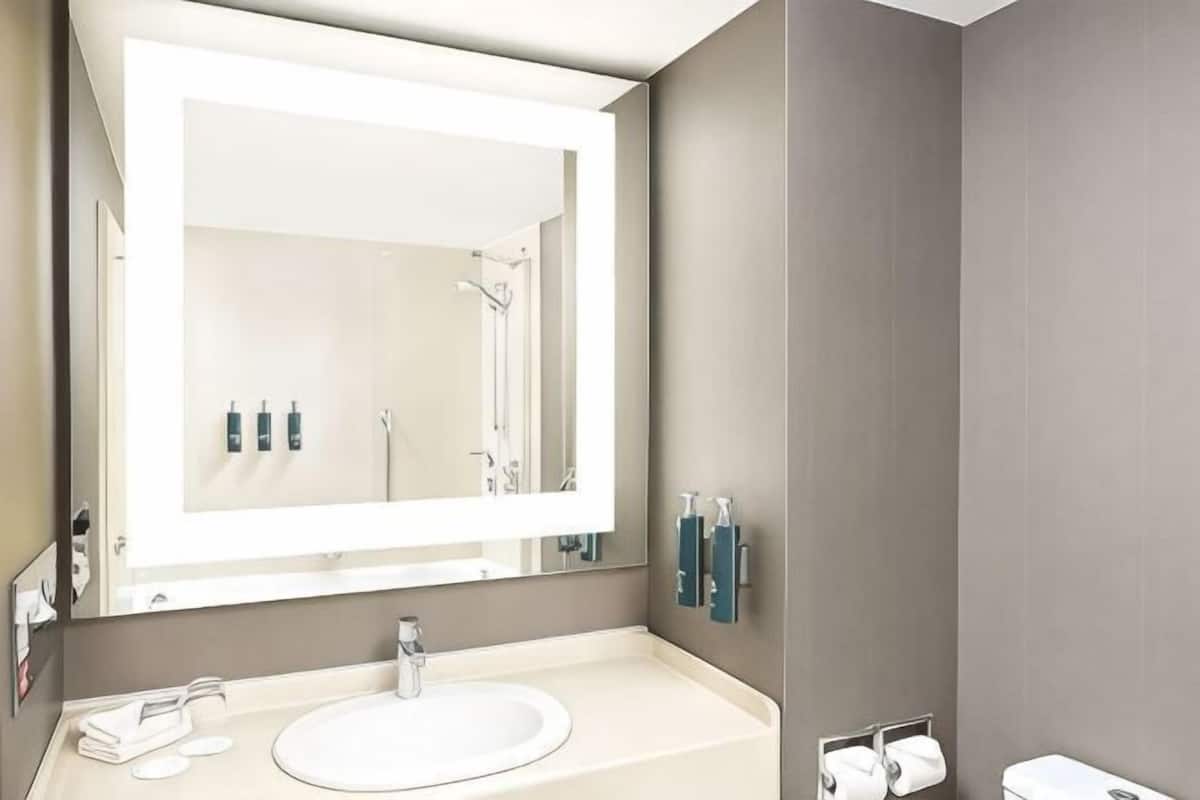 A bathroom with a large mirror, a sink, a toilet, and a towel rack.