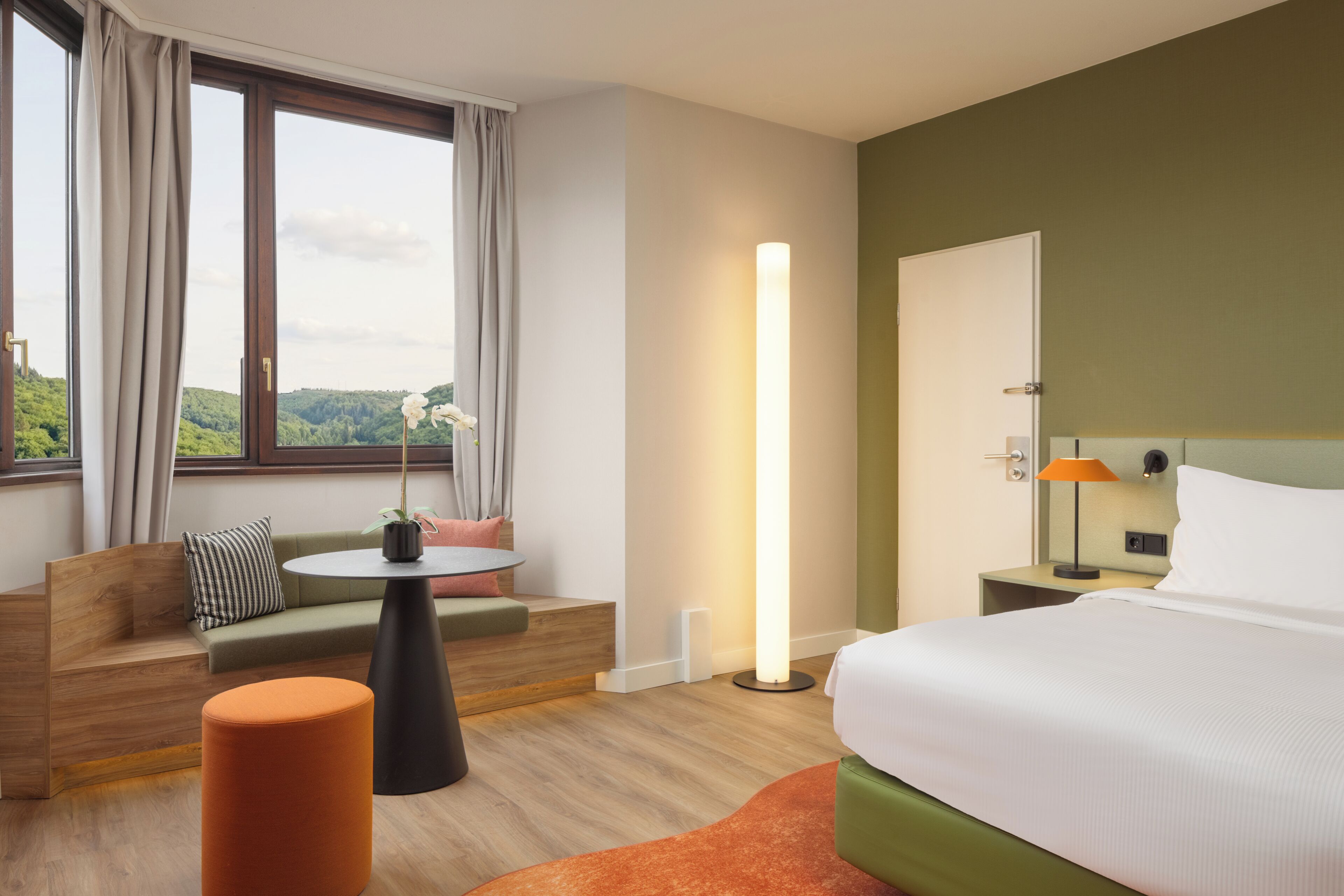 Une chambre d’hôtel avec un lit, un canapé, une petite table, une table de chevet et une fenêtre avec des rideaux.