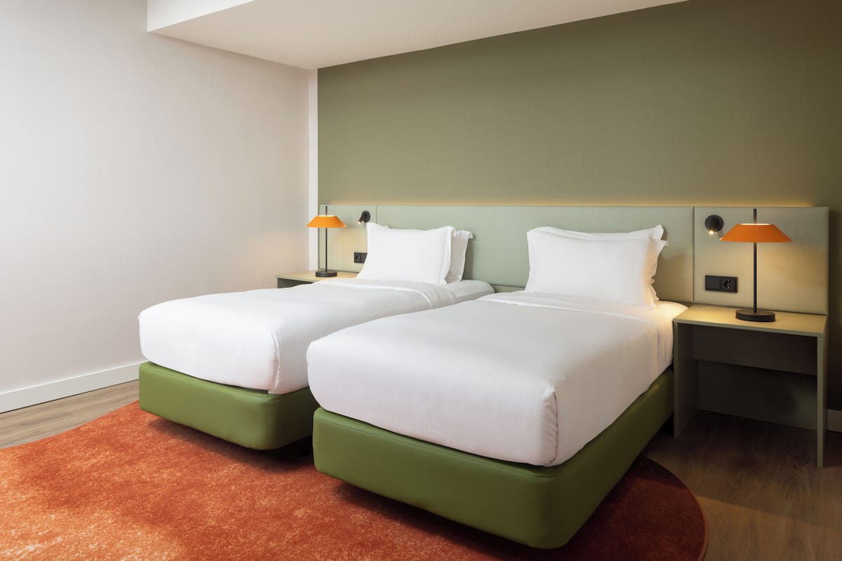 A hotel room with two beds, green headboards, white bedding, and two bedside lamps.