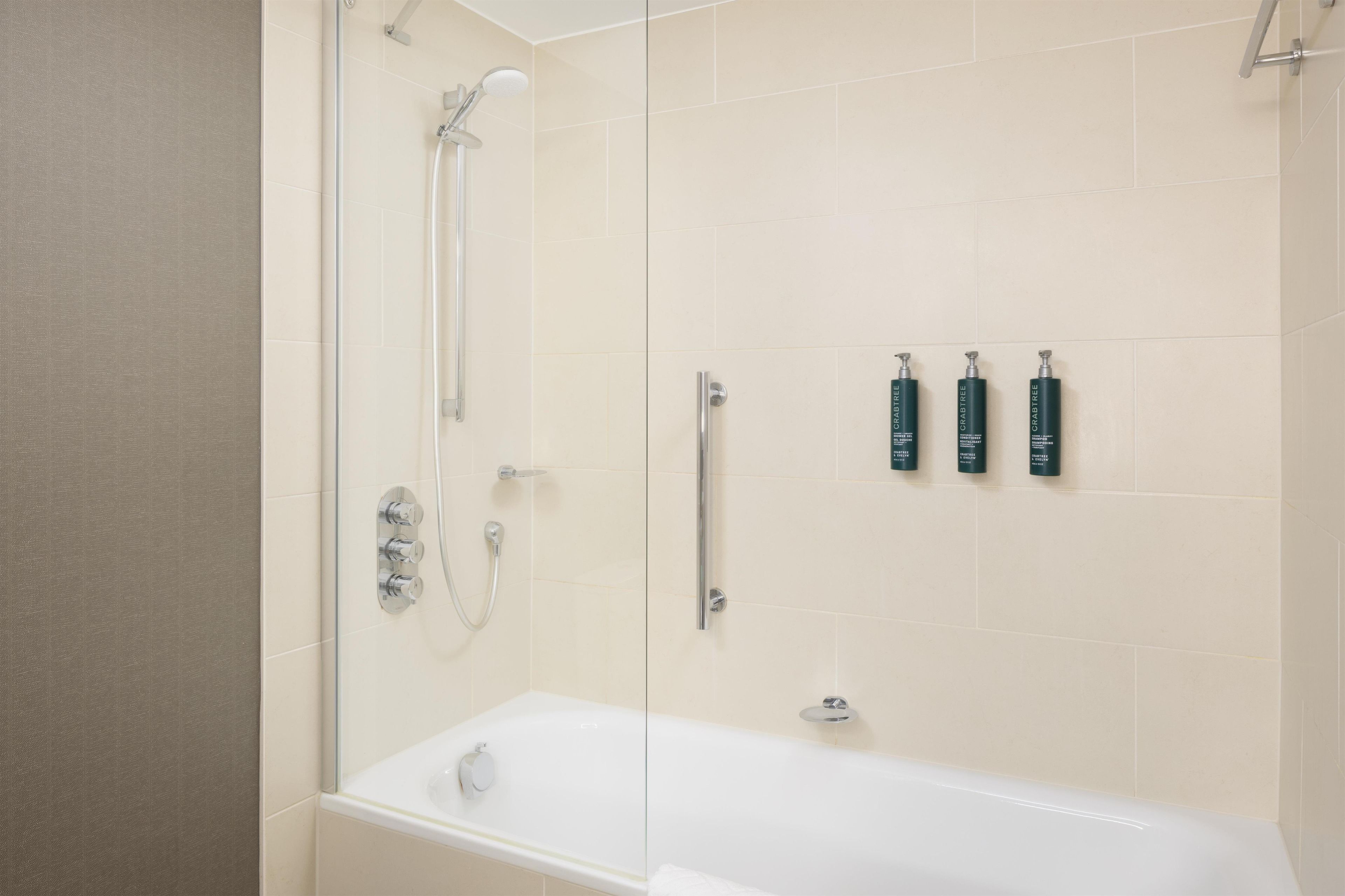 Un baño moderno con cabina de ducha acristalada, una bañera blanca y tres artículos de aseo en la pared.