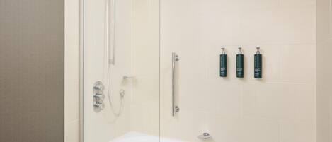 Un baño moderno con cabina de ducha acristalada, una bañera blanca y tres artículos de aseo en la pared.