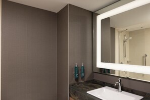 Une salle de bain moderne avec un grand miroir, un lavabo et deux flacons de savon liquide fixés au mur.
