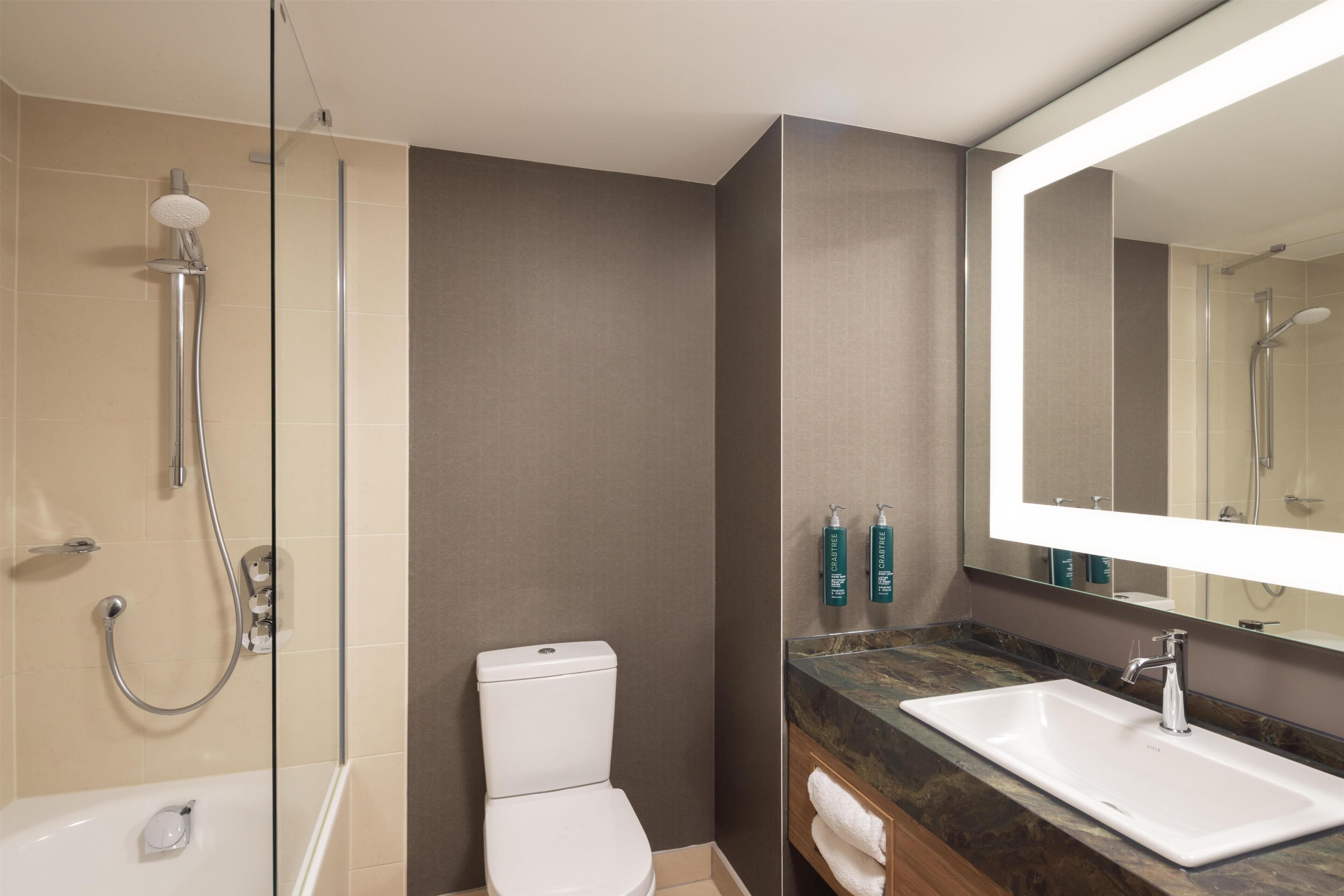 Un baño moderno con ducha envuelta en vidrio, inodoro blanco, un espejo grande y encimera de mármol.