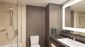 A modern bathroom with a glass-enclosed shower, a white toilet, a large mirror, and a marble countertop.