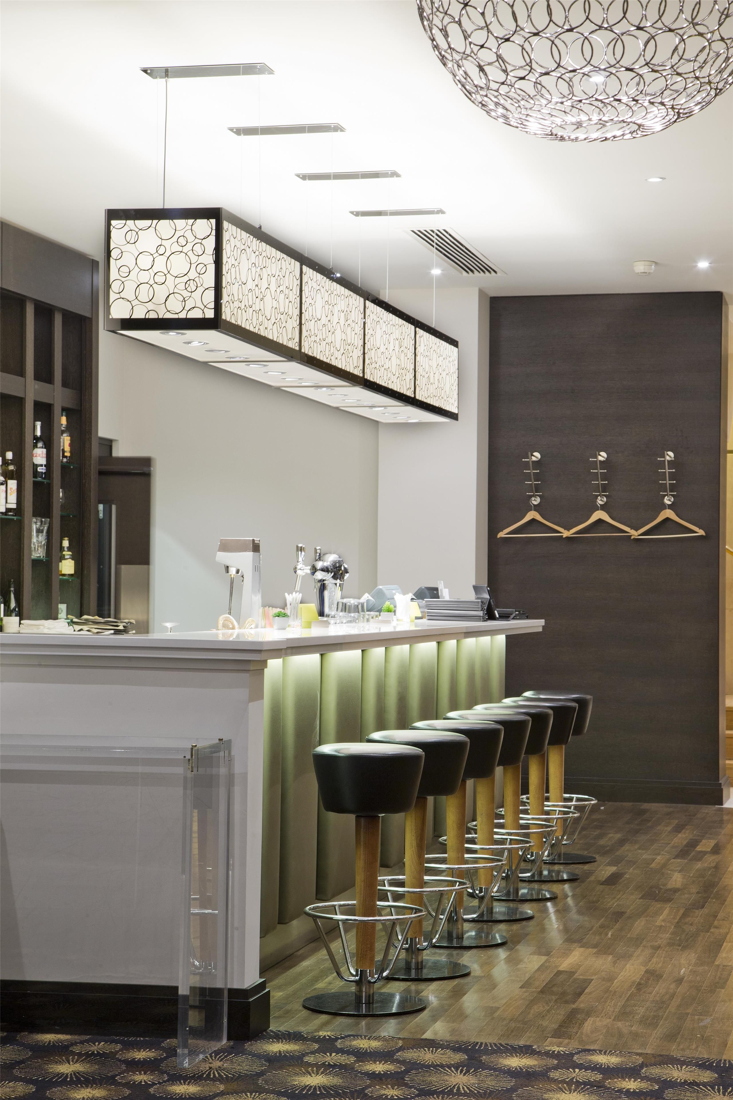 A modern bar area with a long counter, bar stools, and a decorative ceiling light.