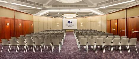 A conference room with rows of chairs, a carpeted floor, a chandelier, and a sign reading 'DOUBLETREE by Hilton'.