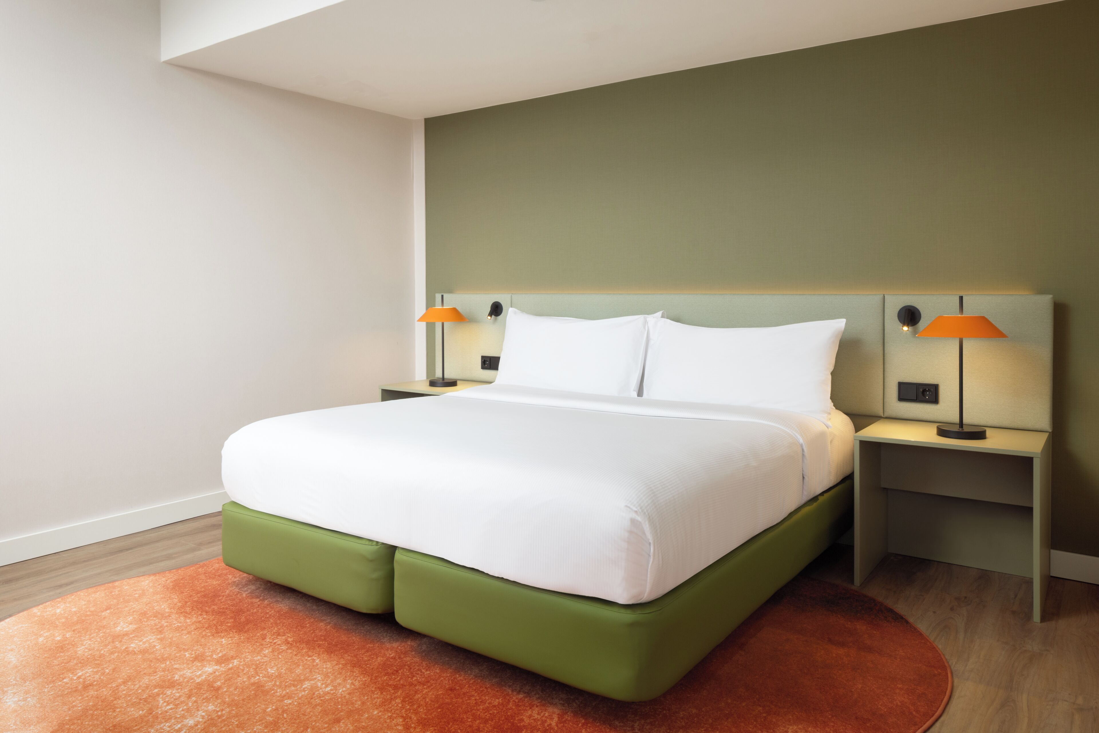 A neatly made bed with white linens, two bedside lamps, and a green headboard.