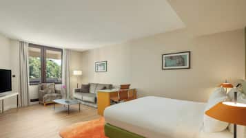 A hotel room with a bed, a desk, a chair, a sofa, a TV, and a window with curtains.