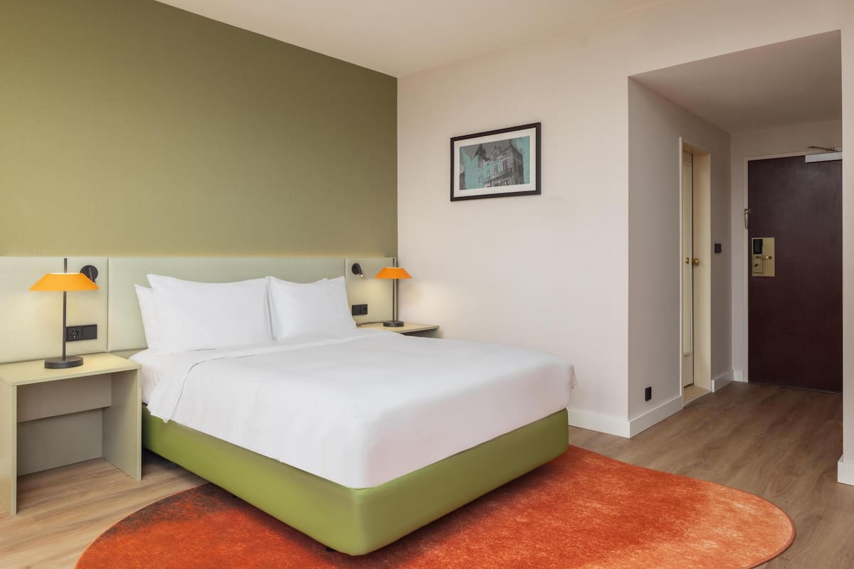 A hotel room with a bed, nightstands, a lamp, a framed picture on the wall, and a door.