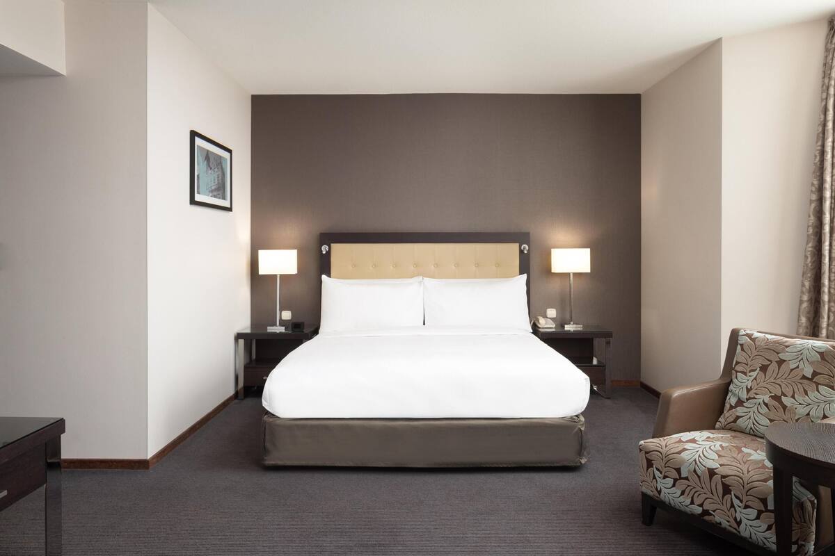 A hotel room with a large bed, two bedside tables with lamps, a chair, and a small table.