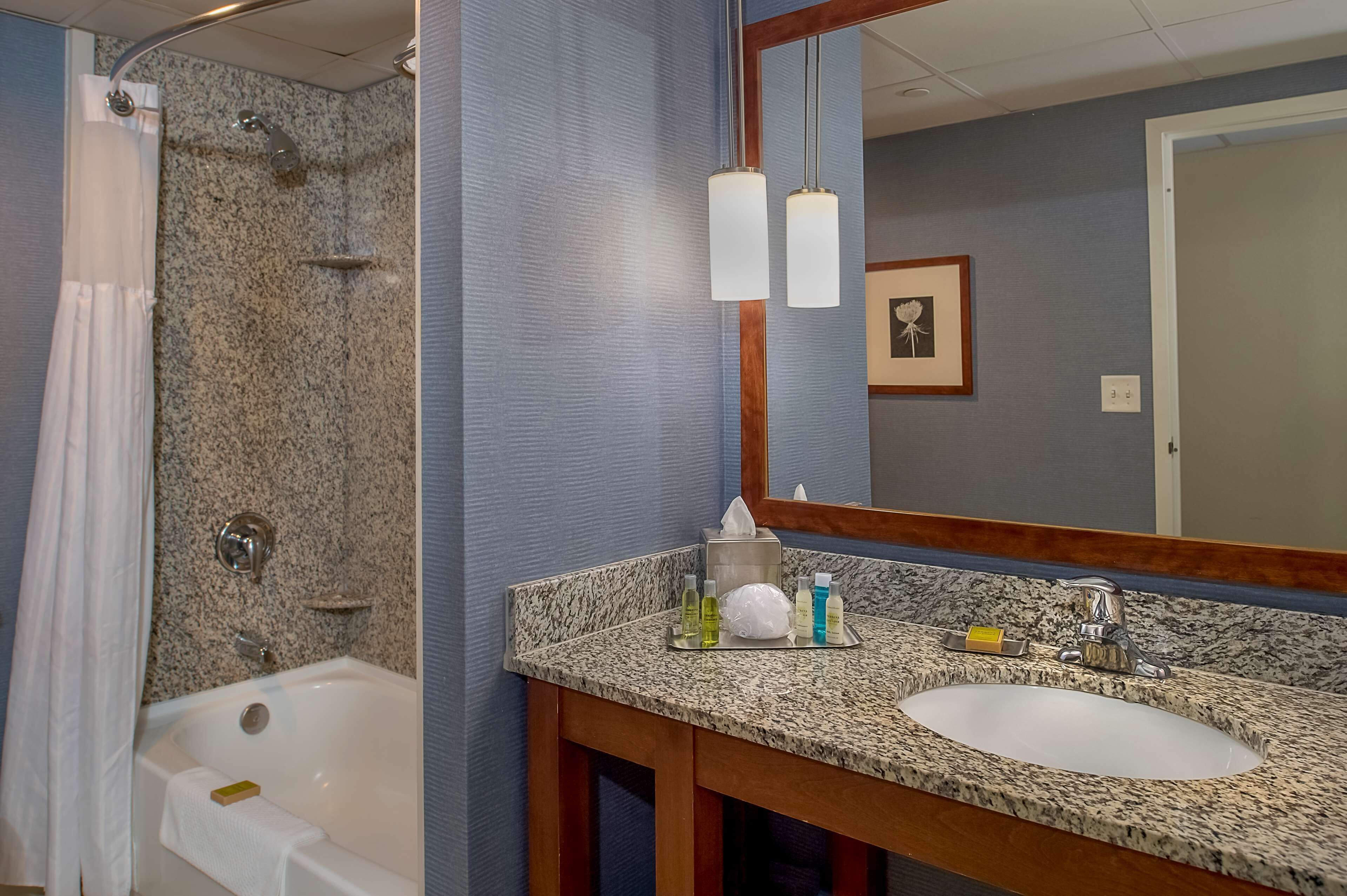 A bathroom with a granite countertop, a white sink, a shower with a curtain, and a mirror with two light fixtures.