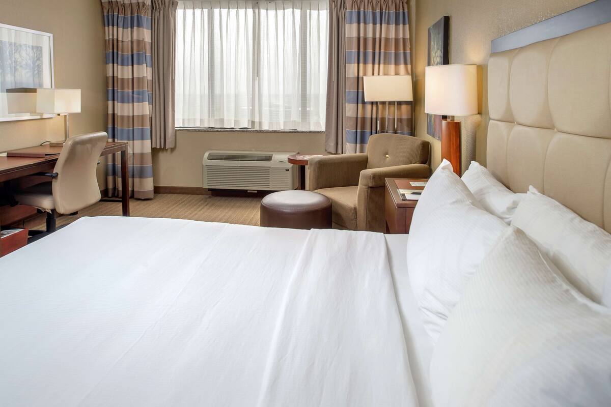 Habitación de hotel con una cama grande, un escritorio con una silla, una mesita y una lámpara.