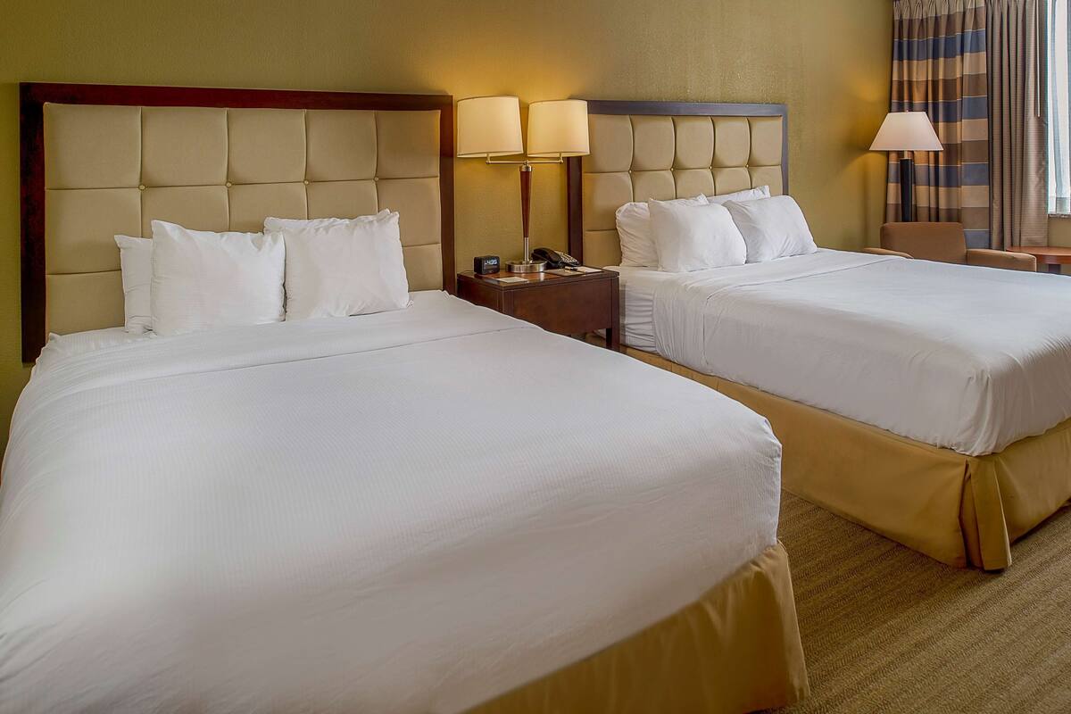 Dos camas tamaño queen con cabeceras, mesitas de noche con lámparas y vistas a una ventana con cortinas.