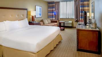 Habitación de hotel con una cama grande, un escritorio con computadora, una silla, una lámpara y una ventana con cortinas.