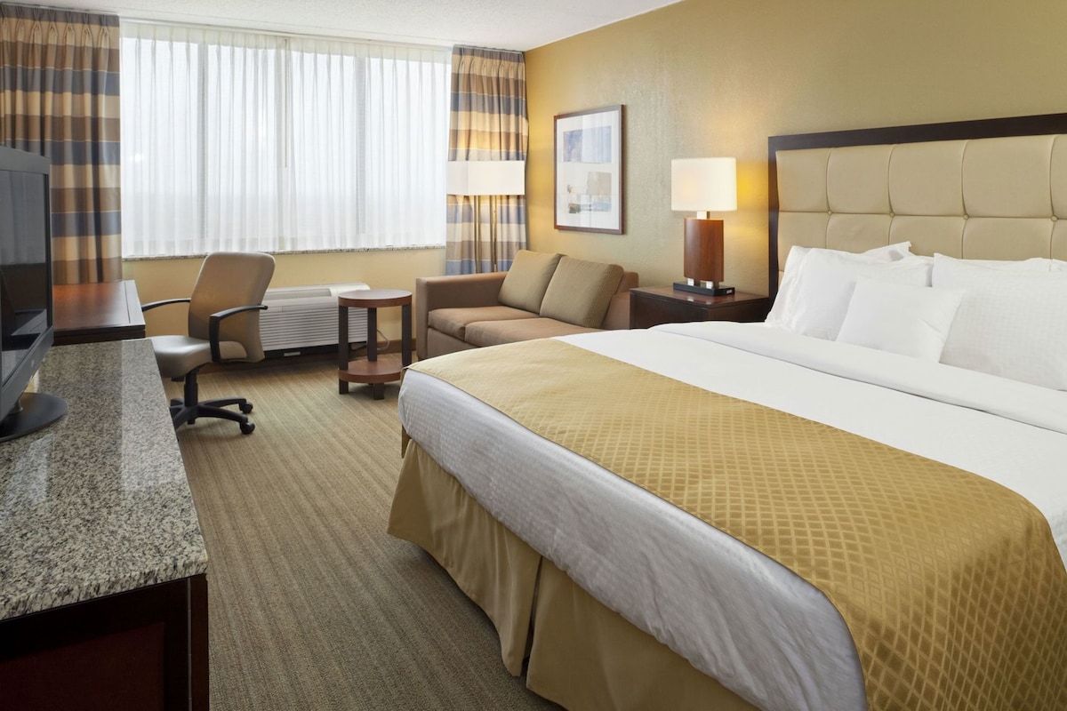 A hotel room with a bed, a desk, a chair, a lamp, and a picture on the wall.