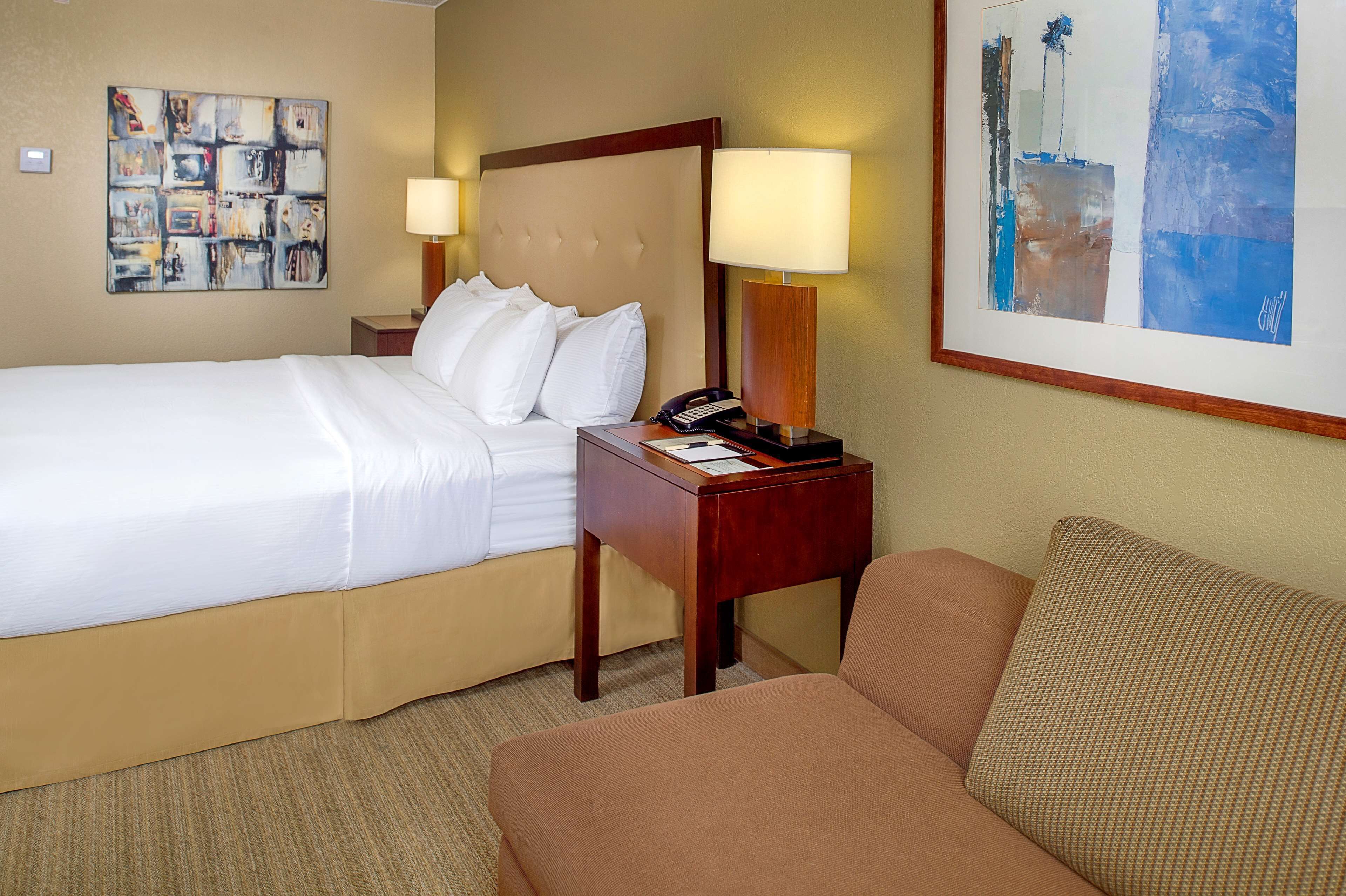 Una habitación de hotel con una cama, una mesita de noche, una lámpara, un teléfono y un sofá.