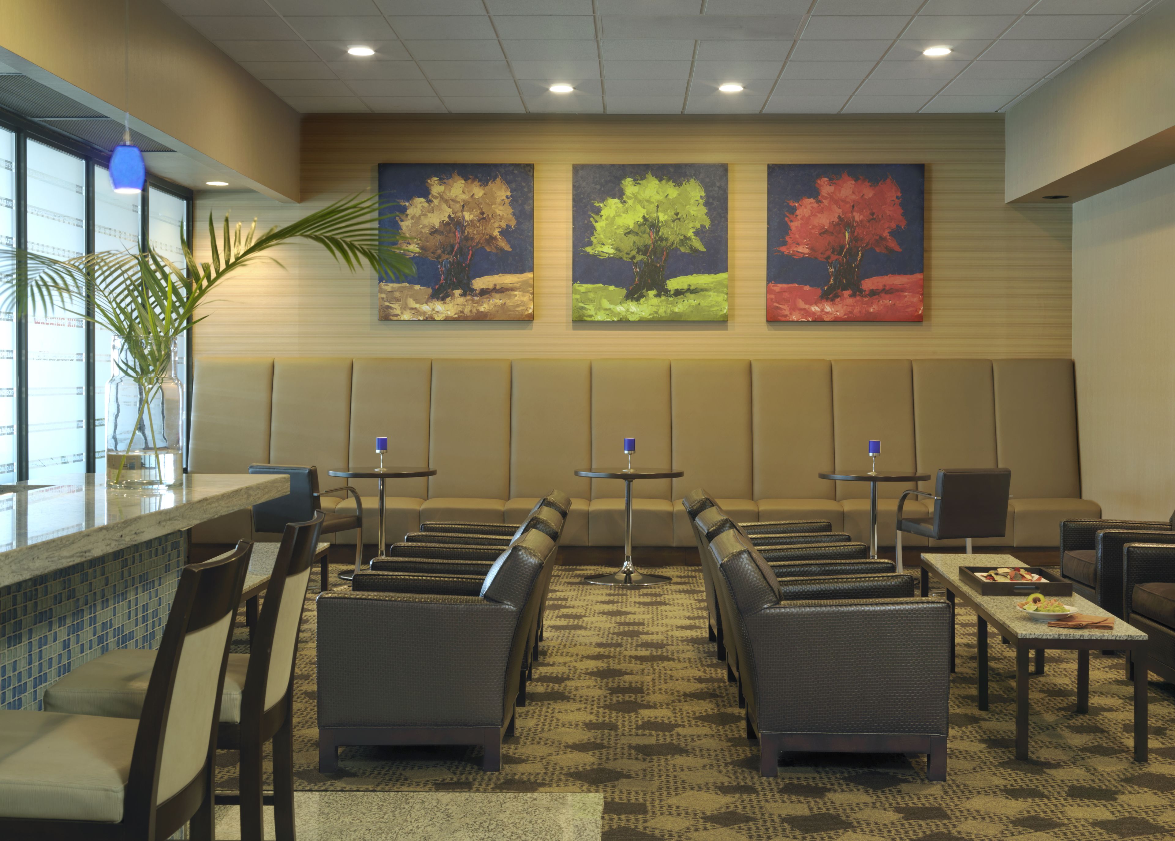 A hotel lobby with seating areas, a reception desk, and three large paintings on the wall.