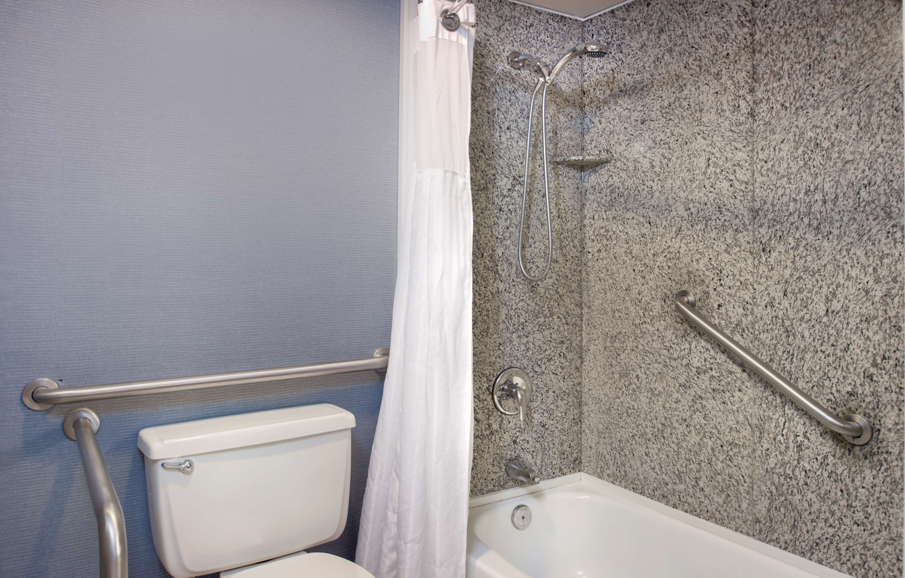 Un baño con ducha, barras de apoyo, inodoro y bañera.