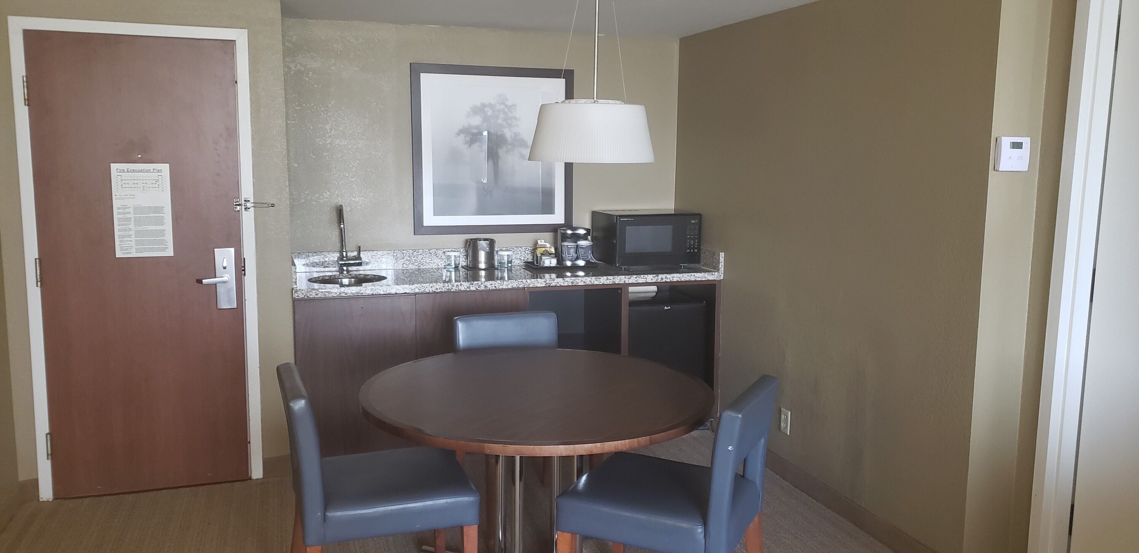 A small dining area with a round table, two chairs, a microwave, a coffee maker, and a framed picture on the wall.