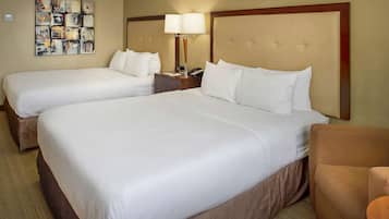 A hotel room with two beds, a nightstand with a lamp, and a small seating area.