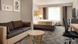 A hotel room with a sofa, a bed, a desk with a chair, and a television.