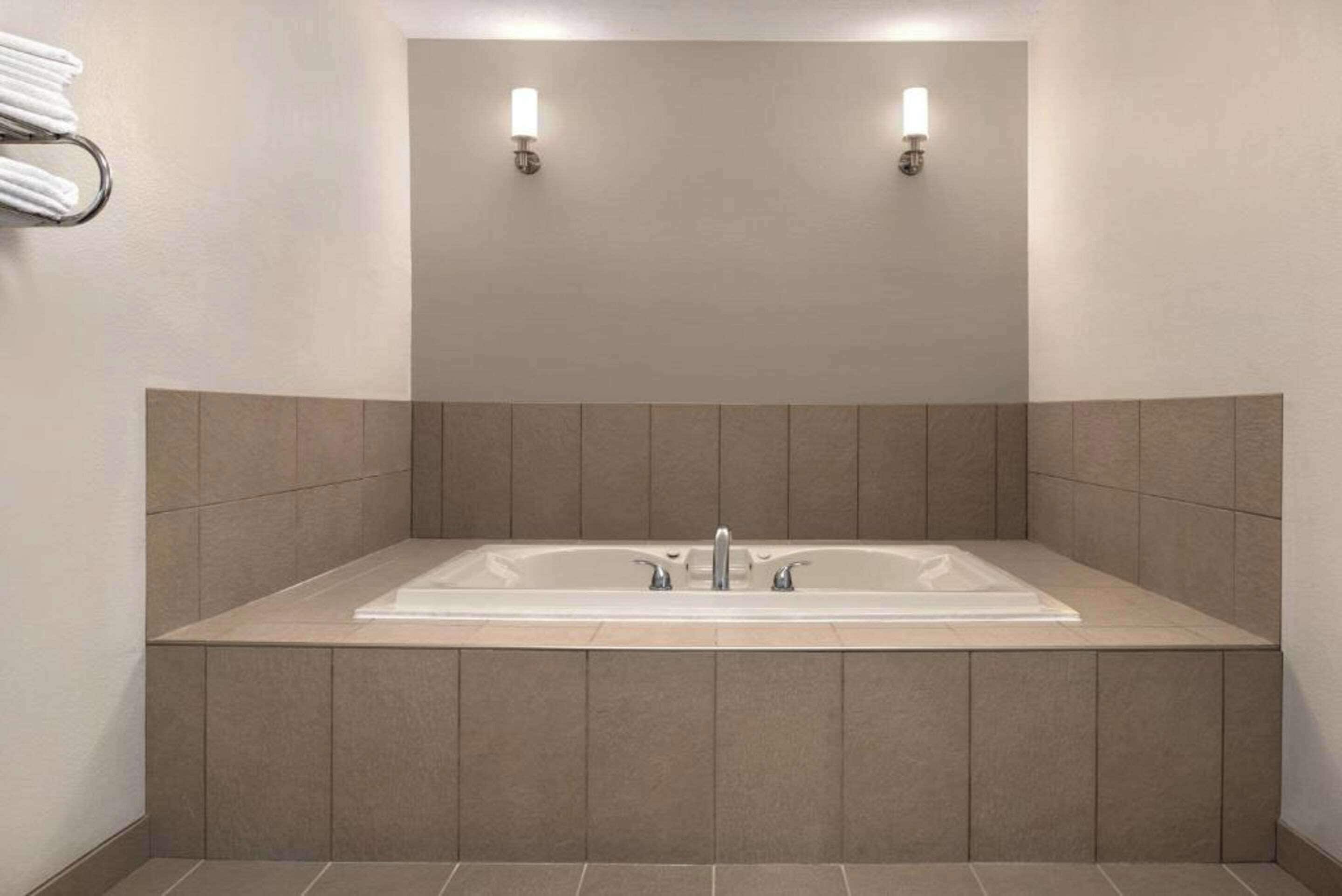 A modern bathroom with a large rectangular bathtub, two wall-mounted light fixtures, and a towel rack.