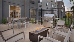 An outdoor patio with a grill, seating, and a fire feature.
