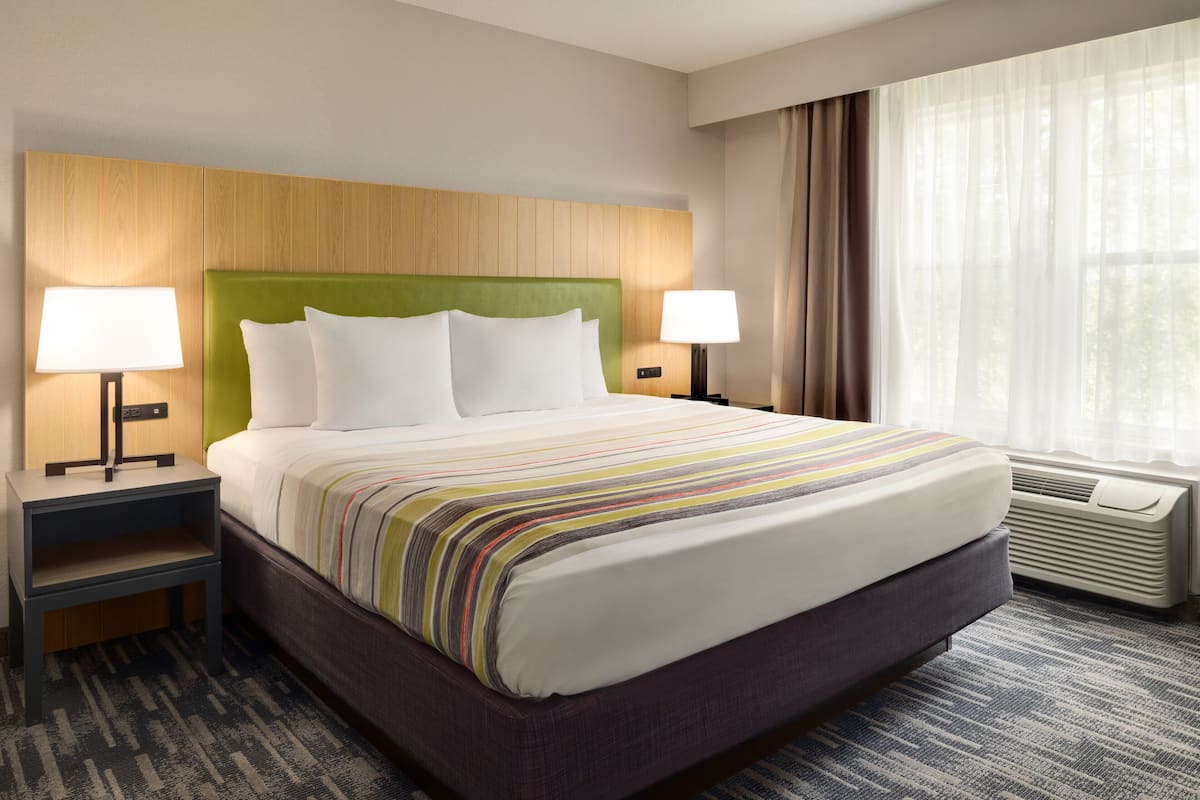 Een hotelkamer met een groot bed, twee nachtkastjes met lampen, een hoofdeinde en een raam met gordijnen.