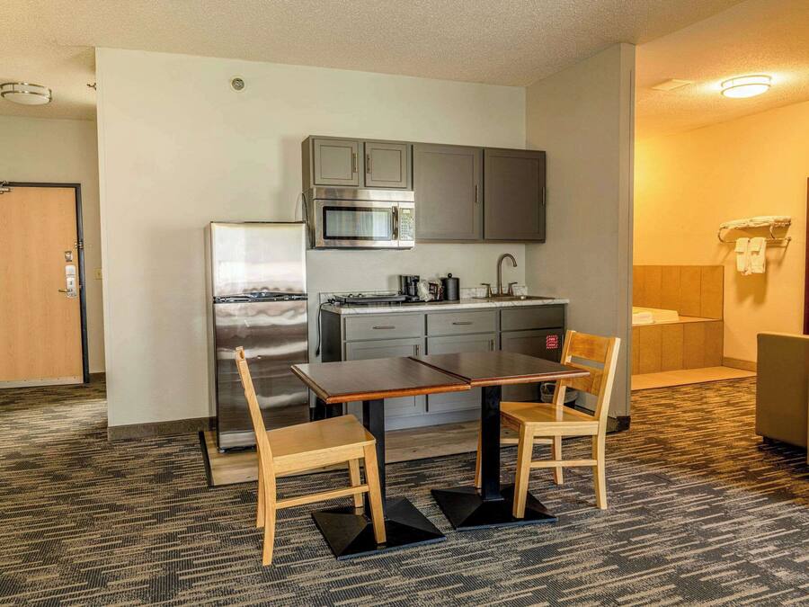 Cocina compacta con microondas, estufa y armarios, una pequeña mesa de comedor con sillas y piso alfombrado.