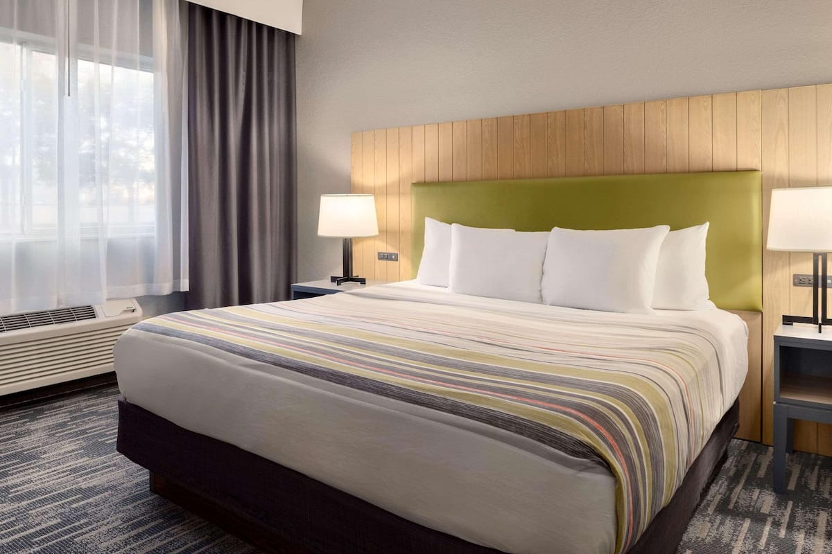 Een hotelkamer met een groot bed, een houten hoofdbord, twee bedlampjes, een raam met gordijnen en een vloerbedekking.