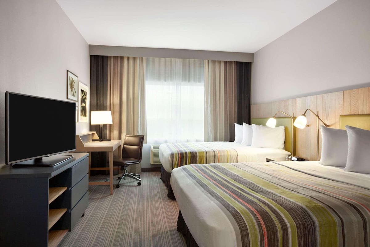 Hotelkamer met flatscreen-televisie, bureau met stoel, twee bedden, groot raam met gordijnen en een hoofdeinde met lampen.