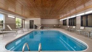 An indoor swimming pool with a wooden ceiling, tiled floor, and lounge chairs around the perimeter.