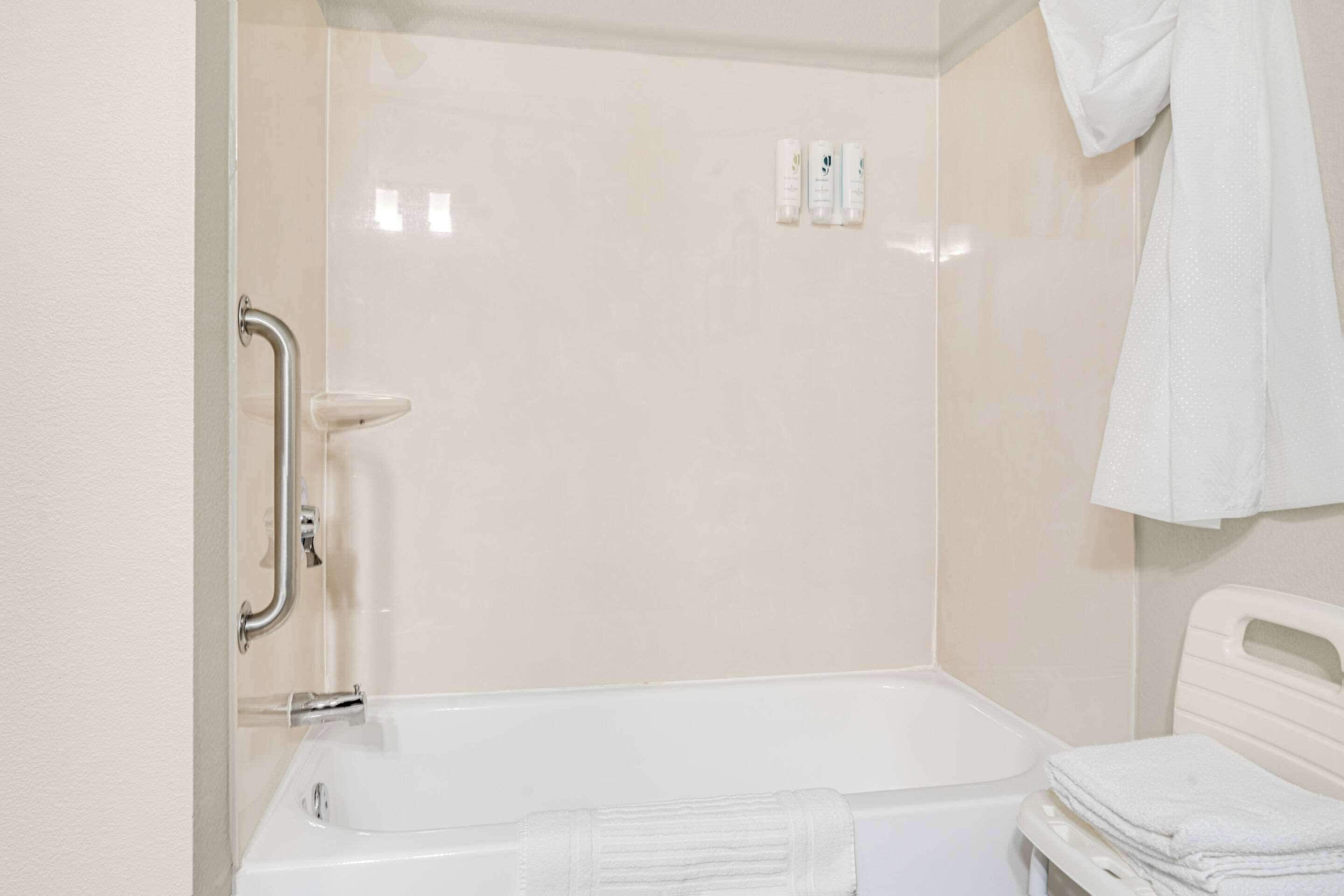 A bathroom with a bathtub, a handrail, and a stack of white towels.