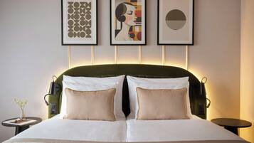 A neatly made bed with two pillows, a bedside table with a vase, and three framed artworks on the wall.