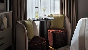 Een moderne hotelkamer met een ronde tafel, twee fauteuils, een bank, een lamp en een raam met gordijnen.