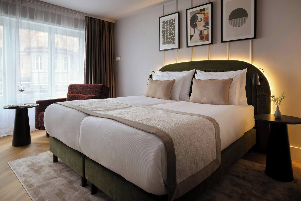 Een moderne hotelkamer met een groot bed, een stoel, een tafeltje en kunst aan de muur.