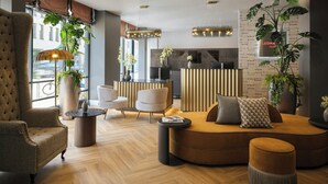 Een moderne hotellobby met een bank, fauteuils, een receptiebalie en grote ramen.