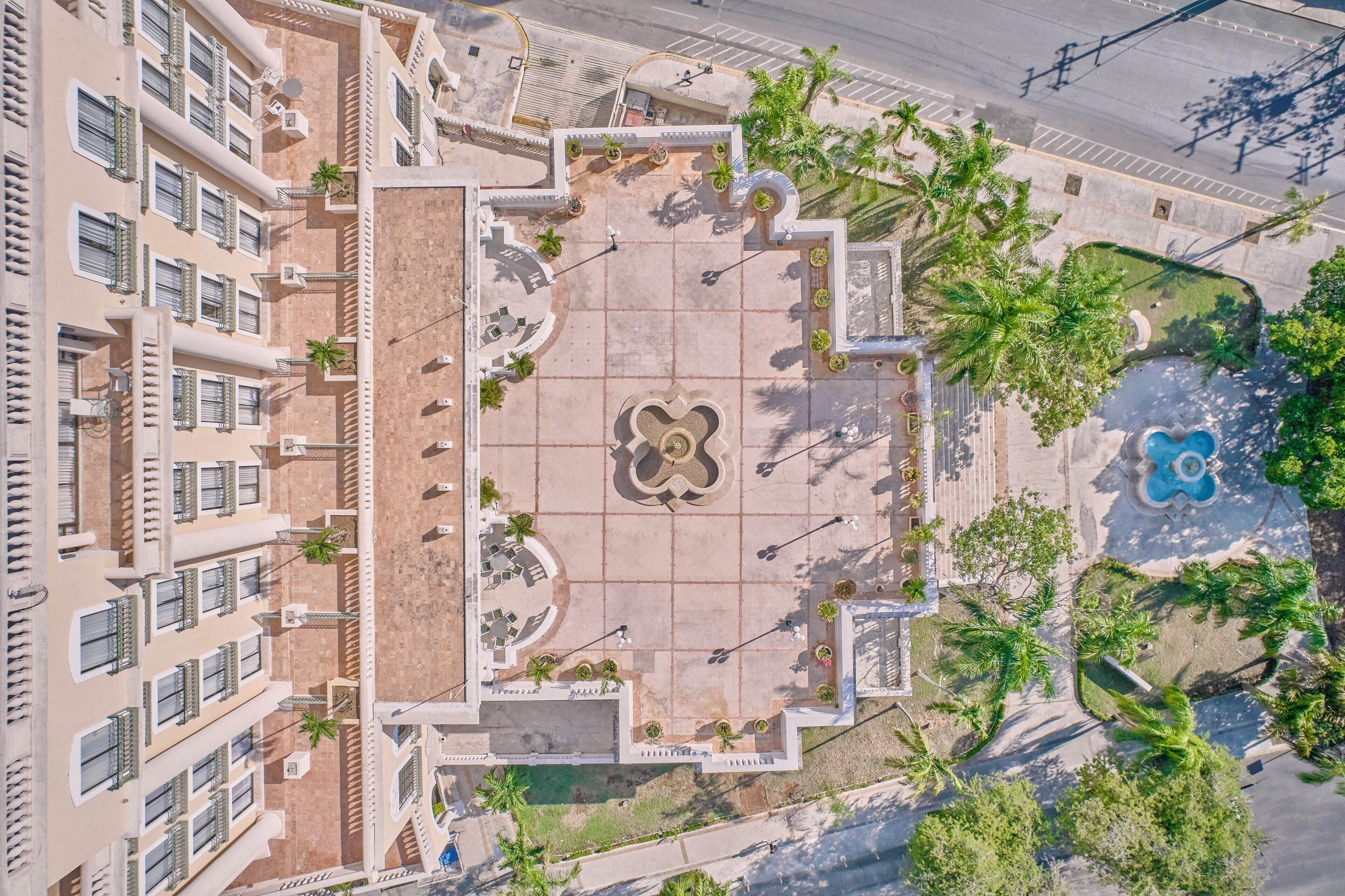 Vue aérienne d’une cour d’hôtel avec une fontaine centrale, des palmiers tout autour et une piscine.