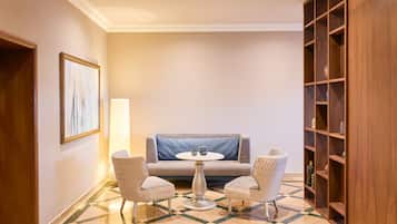 A hotel room with a checkered floor, a sofa, two patterned chairs, a small round table, and a bookshelf.