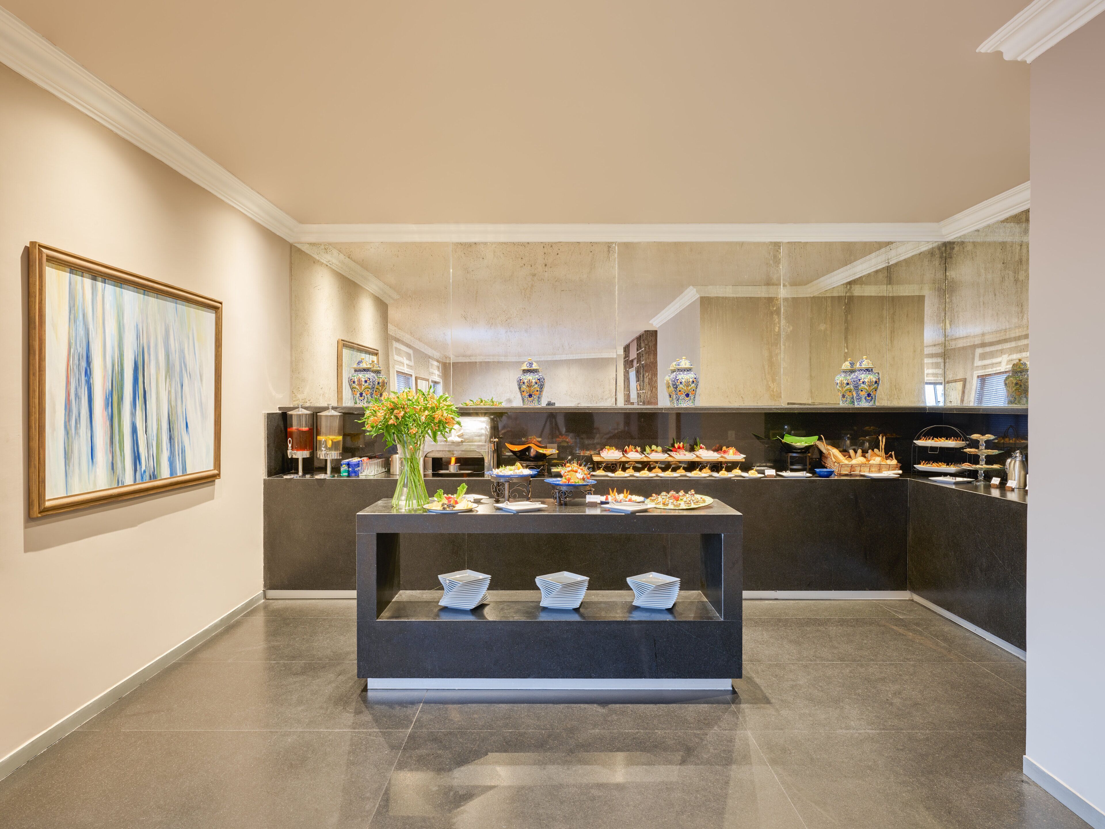Un moderno vestíbulo de hotel con una recepción, un cuadro abstracto grande y una zona de bufé con diferentes opciones de comida.