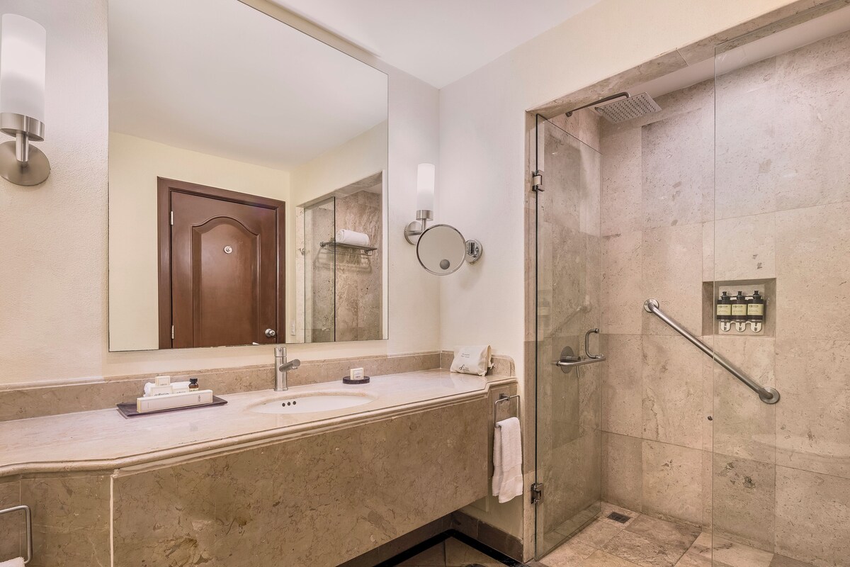 A hotel bathroom with a large mirror, a sink, a shower with a glass door, and a towel rack.