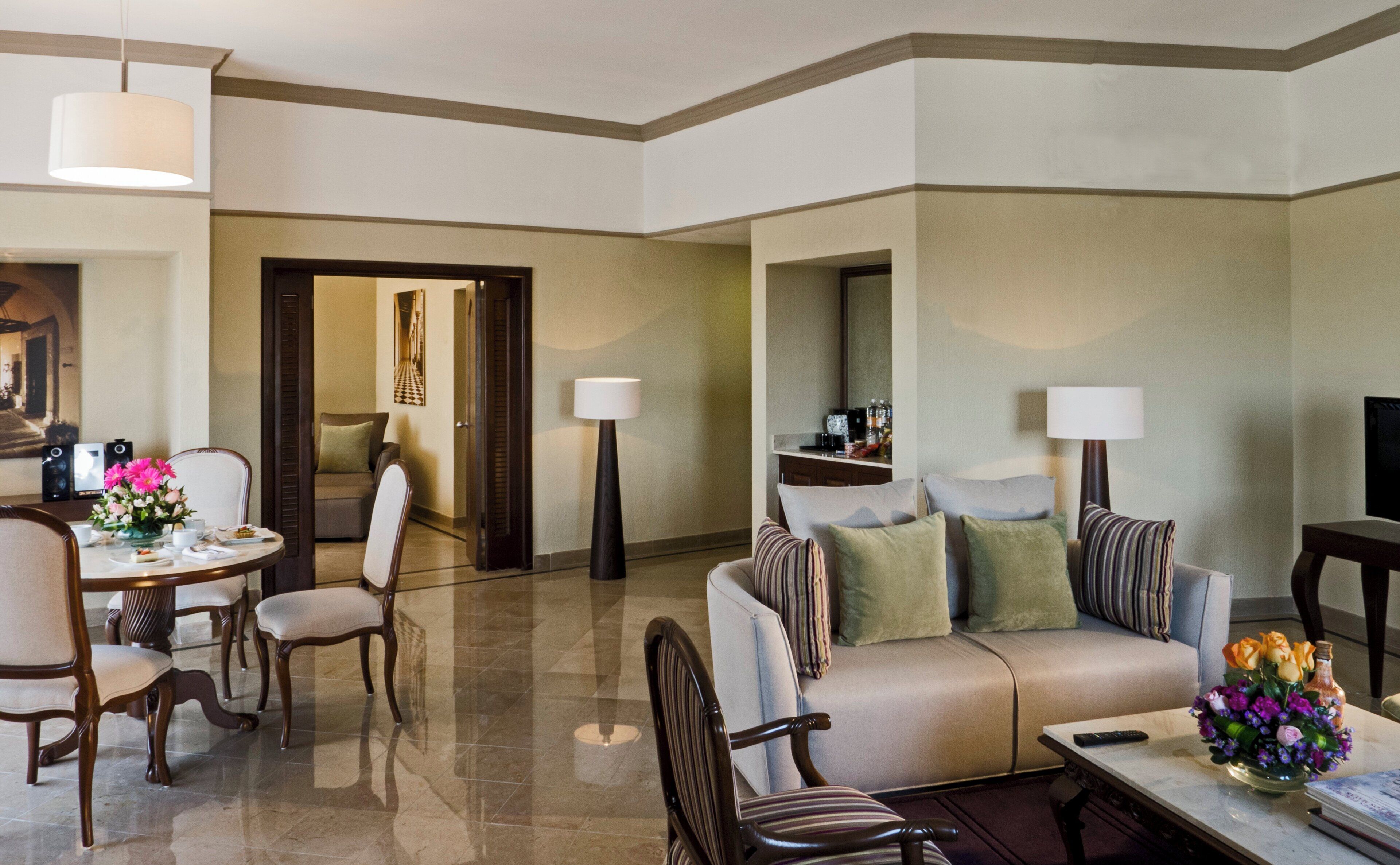 Habitación de hotel con comedor, sofá, mesa de centro y televisor.