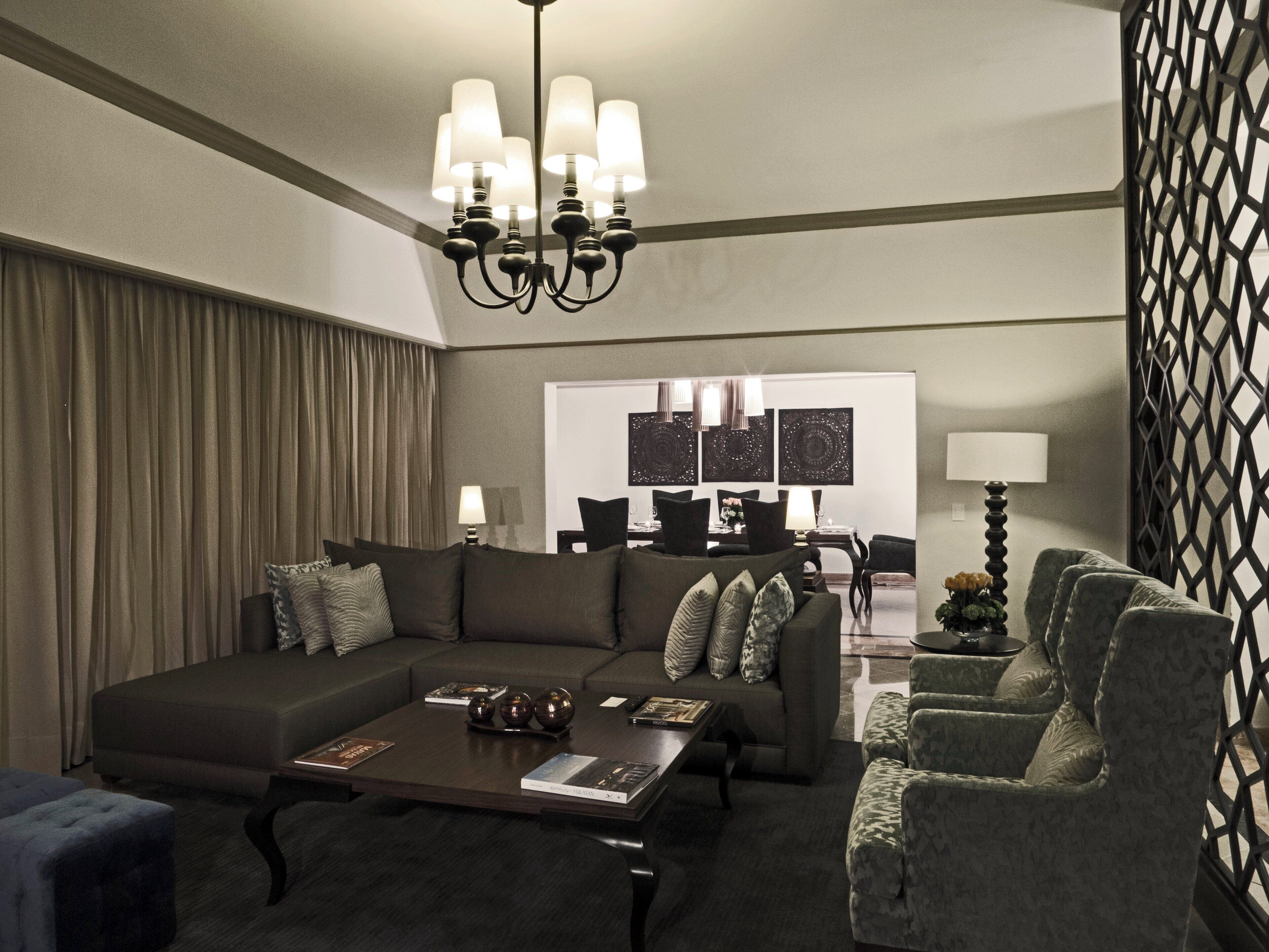 A modern living room with a dark-colored sofa, matching armchairs, a coffee table, and a chandelier.