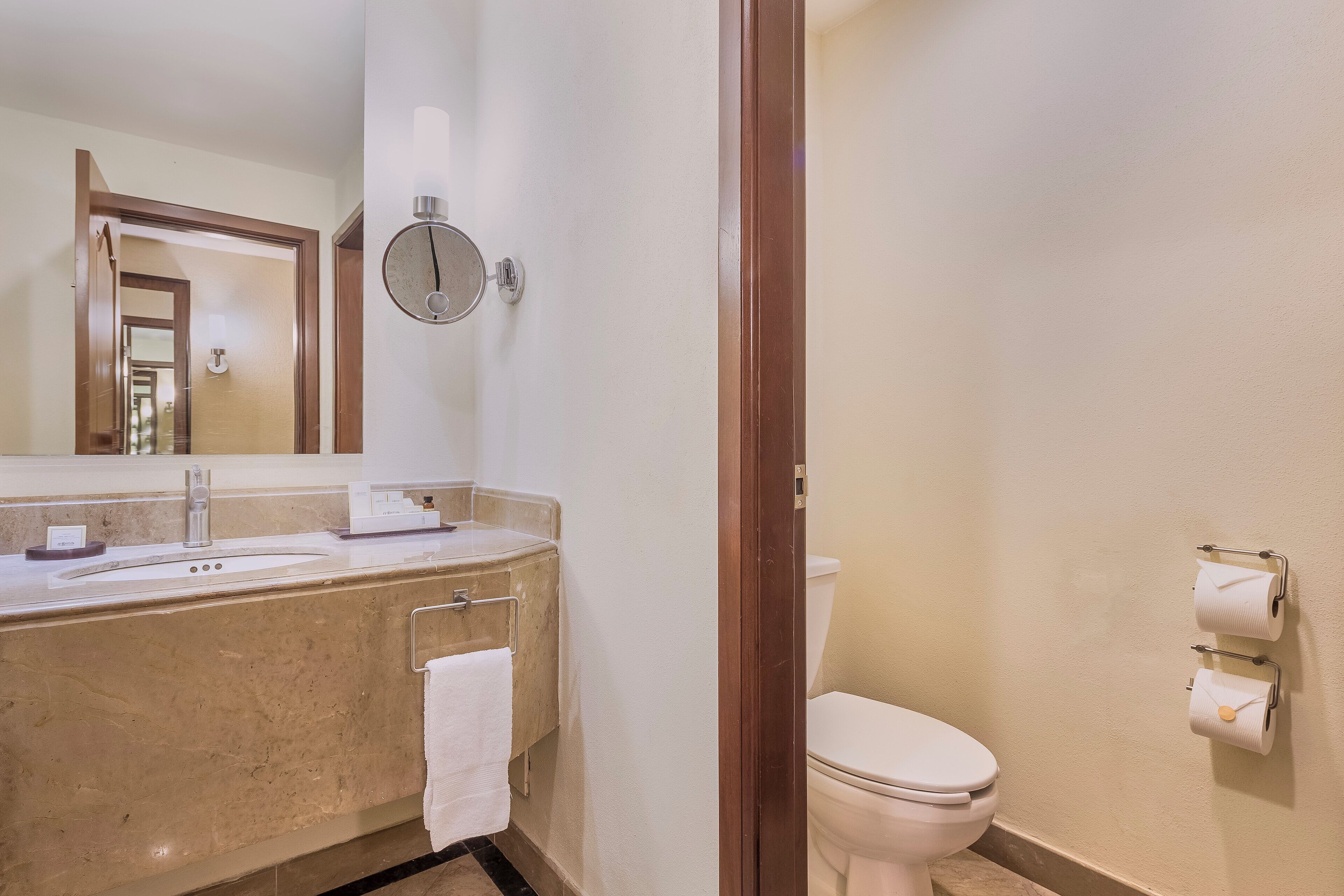 A bathroom with a sink, mirror, towel rack, toilet, and toilet paper holder.