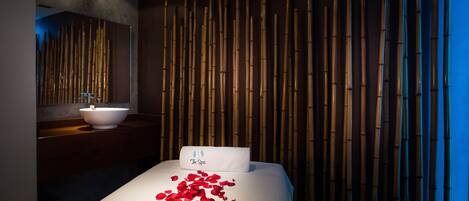 A modern spa room with a bed, a white pillow, and a wall of vertical bamboo panels.